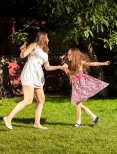 brunette woman an young girl holding ands and dancing at yard